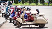 Tematinė nuotrauka: senovinis „Vespa“ motoroleris, važiuojantis siaura Italijos gatve