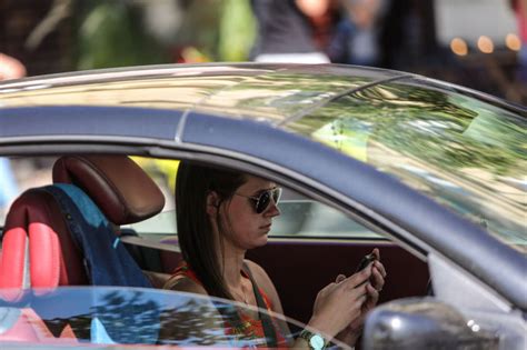 Teminė nuotrauka: vairuotojas su mobiliuoju telefonu rankoje už vairo, pabrėžianti išsiblaškymą