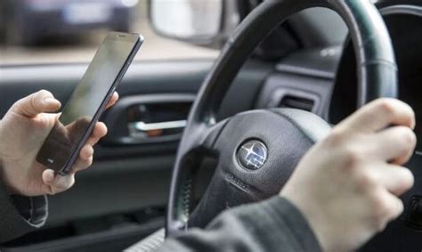 Teminė nuotrauka: vairuotojas už vairo, naudojantis mobiliuoju telefonu, su įspėjamaisiais ženklais fone