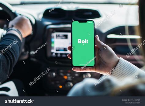 Thematic photo of a person driving a car and holding a smartphone with a Bolt app