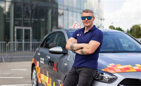 Vairavimo instruktorius su mokiniais prie mokomojo automobilio