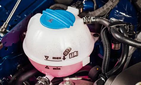 butelis su distiliuotu vandeniu šalia automobilio aušinimo sistemos komponentų