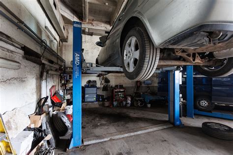 Teminis foto: automobilių servisas, meistras remontuoja duslintuvą ant keltuvo