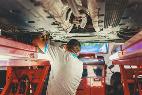 Automobilio apžiūra servise: mechanikas su planšete tikrina dugną ant keltuvo