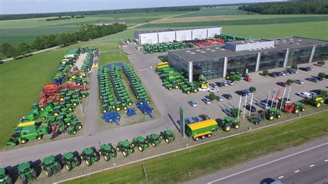 Dainininkė Vaida Genytė sėdinti dideliame, ryškiai žaliame moderniame traktoriuje DOJUS agro centro atidarymo metu. Galima pavaizduoti ir žaismingą perspektyvą, kurioje smulki moteris valdo galingą mašiną.