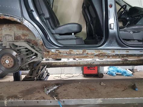 Teminė nuotrauka, vaizduojanti automobilio kėbulo remonto dirbtuves su specialistu, dirbančiu prie automobilio durelių