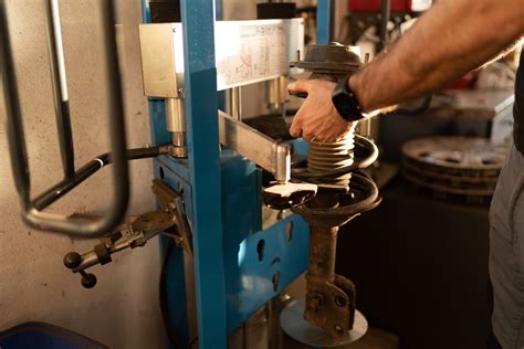 Mechanikas naudoja hidraulinį presą sailenblokui įpresuoti į automobilio pakabos detalę.