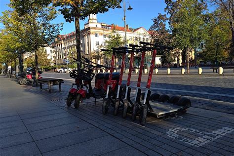 Tematinė nuotrauka, vaizduojanti žmones, važiuojančius elektriniais paspirtukais ir dviračiais mieste saulėtą dieną