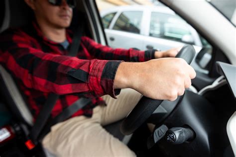 Tematinė nuotrauka: besišypsantis žmogus sėdi prie naujo automobilio šalia autoserviso, fone matyti tvarkomas automobilis