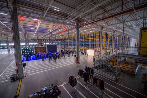 nuotrauka iš šiuolaikinio logistikos centro, kuriame darbuotojas atlieka prekių krovimo darbus