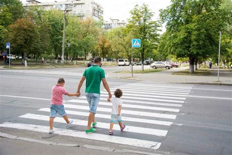 Vaikas su tėvais eina per perėją, stebi šviesoforo signalus