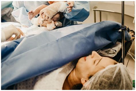 Moters, atsigaunančios po cezario pjūvio, sėdinti lovoje ir švelniai liečianti pjūvio vietą. Gali būti šalia naujagimis.
