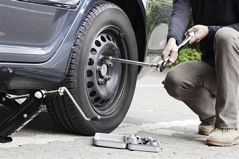 Teminė nuotrauka: žmogus keičia automobilio ratą su hidrauliniu domkratu