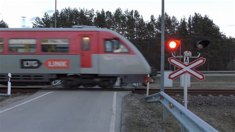 Teminė nuotrauka su geležinkelio pervaža ir artėjančiu traukiniu
