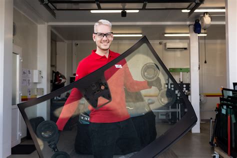 Nuotrauka, vaizduojanti autoserviso meistrą, atliekantį automobilio priekinio stiklo keitimą