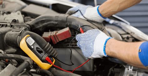 Mechanikas tikrina automobilio akumuliatorių multimetru